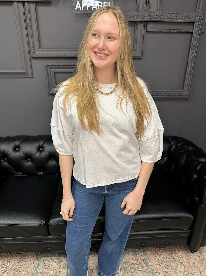 Person wearing a white shirt and blue jeans standing in front of a black leather couch.