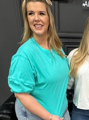Woman wearing a teal shirt standing next to another person indoors.