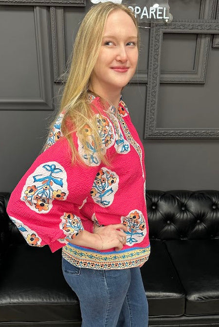 Woman wearing a colorful embroidered blouse and blue jeans standing in front of a black leather couch.