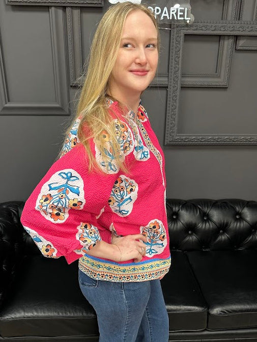 Woman wearing a colorful embroidered blouse and blue jeans standing in front of a black leather couch.