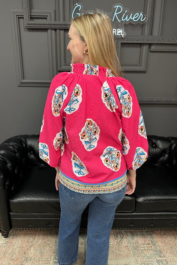 Person wearing a pink blouse with colorful patterns in a room with a black leather couch and gray walls.