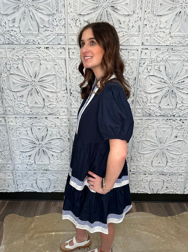 Woman wearing a navy dress with white trim against a decorative tiled wall.
