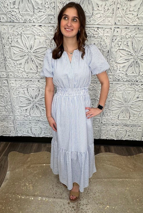 Woman in a white and blue striped dress standing against a decorative tiled wall.