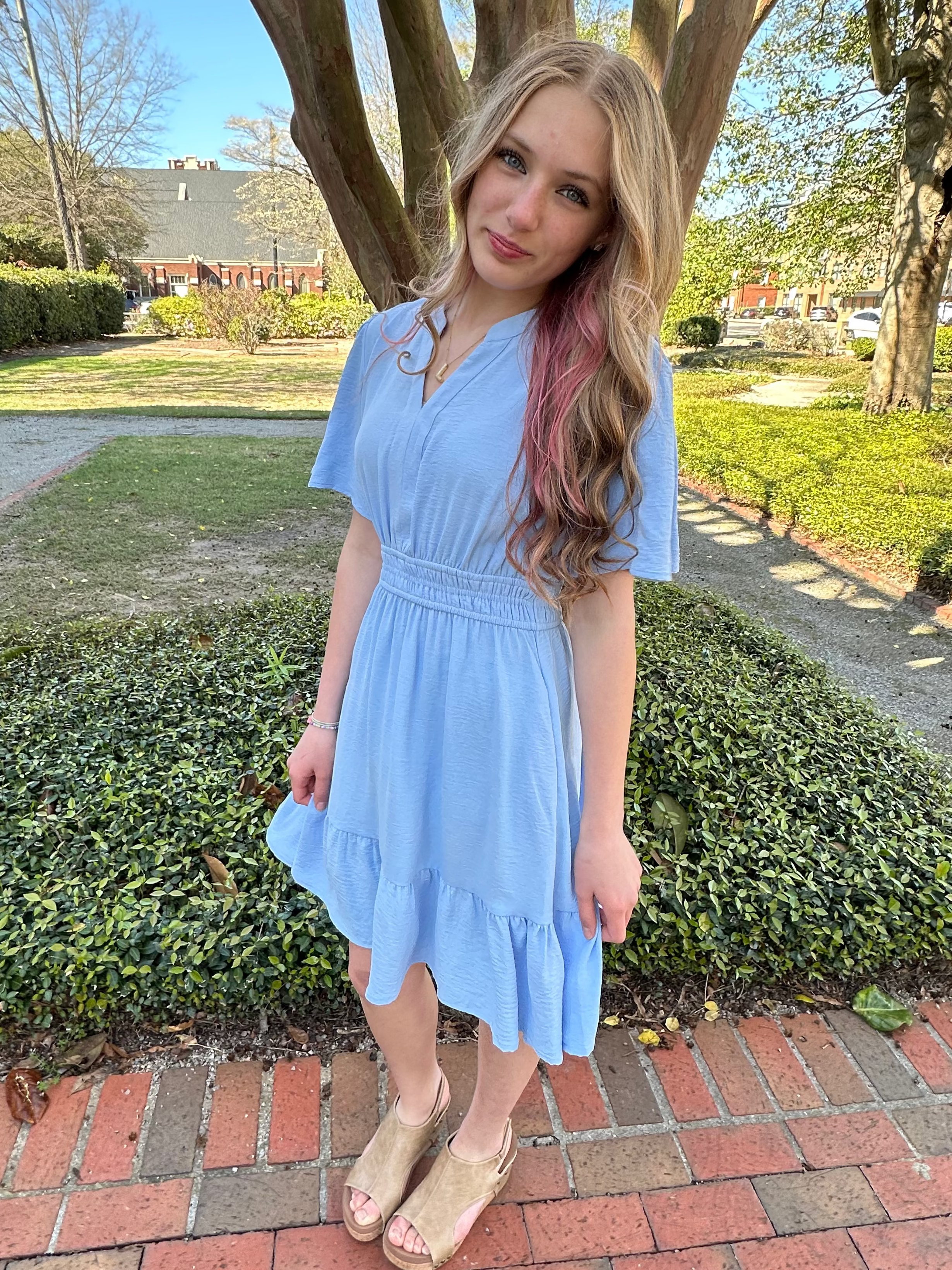 Woman in a light blue dress standing outdoors on a sunny day.
