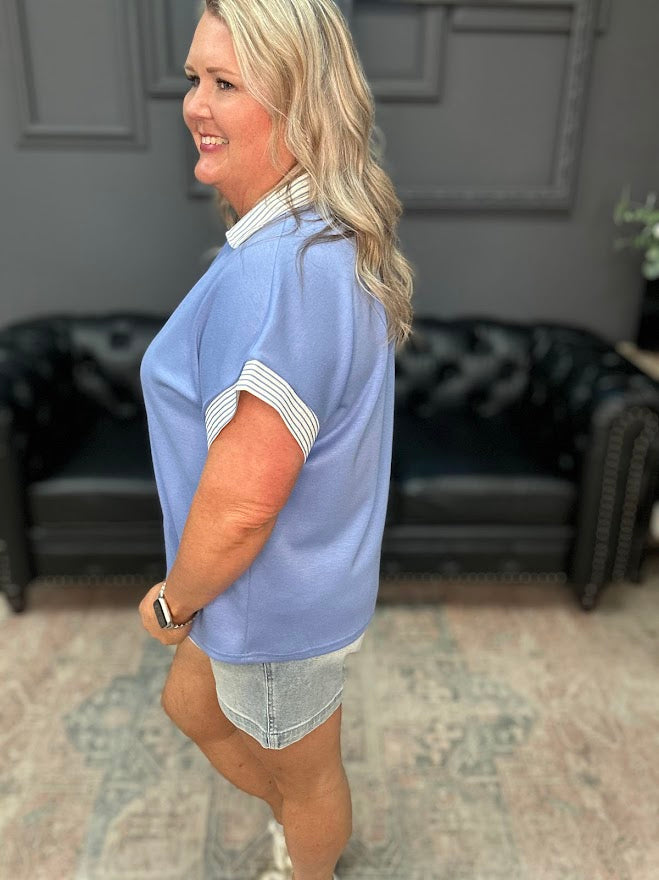 Woman wearing a light blue blouse with white trim in an indoor setting.