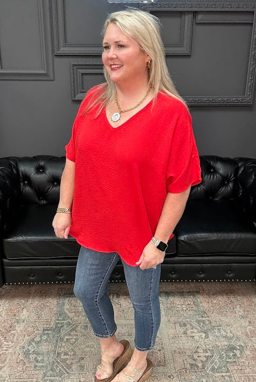 Woman in a red shirt and blue jeans standing in front of a black leather couch.