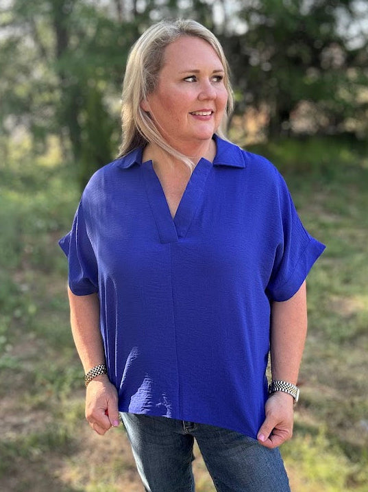 Woman wearing a blue shirt standing outdoors with greenery in the background