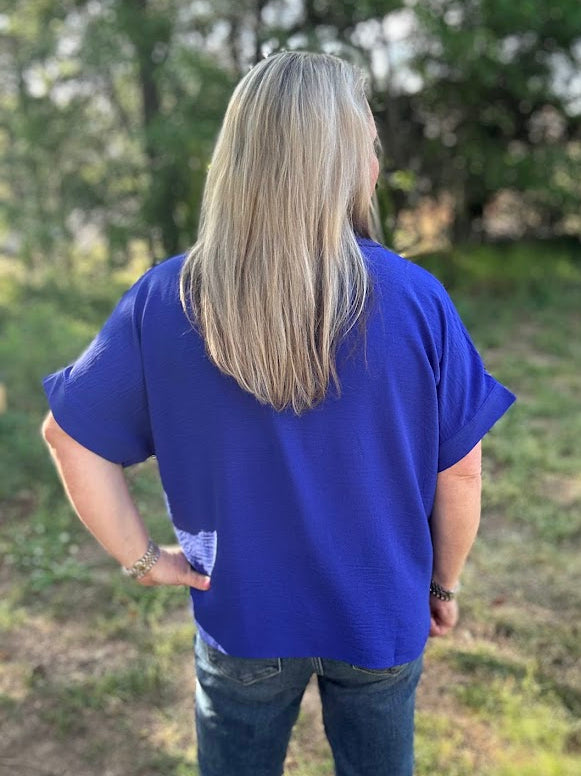 Person wearing a blue shirt standing in a grassy outdoor area with trees in the background