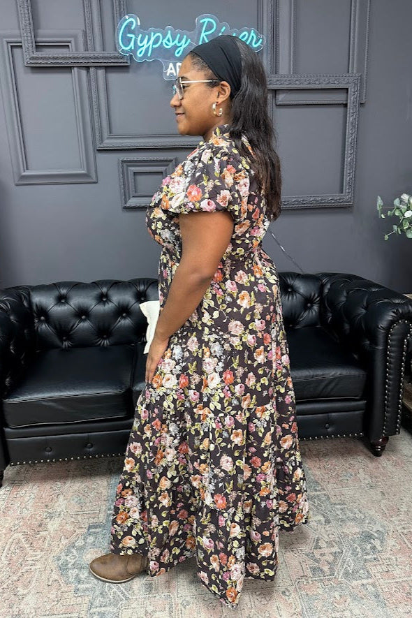 Woman in a floral dress standing in a room with black leather couches and decorative elements.