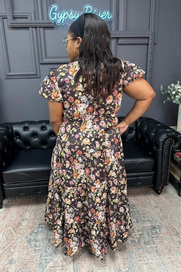 Woman wearing a floral dress in a room with black leather couches and a gray wall.