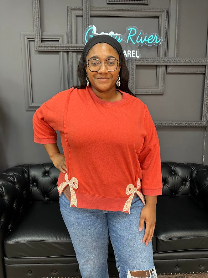 Person wearing an orange top with bow details in a room with a black couch and gray walls.