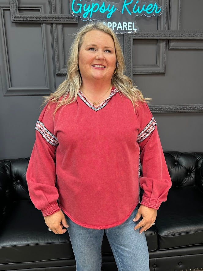 Woman wearing a red long-sleeve shirt with decorative trim in front of a gray wall with 'Gypsy River Apparel' sign.
