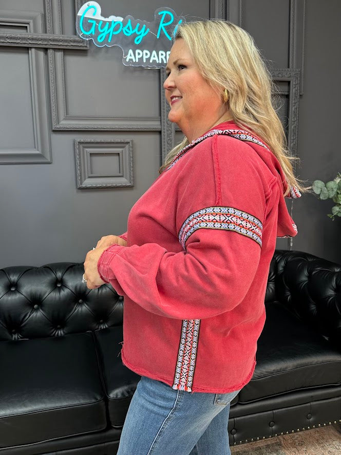 Woman wearing a red hoodie with white patterns in a room with black leather couches and a gray wall.