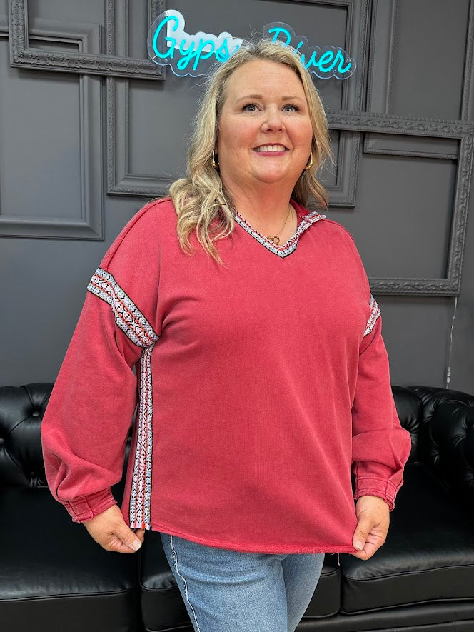 Woman wearing a red sweater with decorative sleeves in a room with a gray wall and black leather couch.