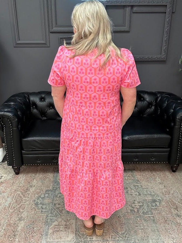 Woman wearing a pink dress standing in a room with a black leather couch.