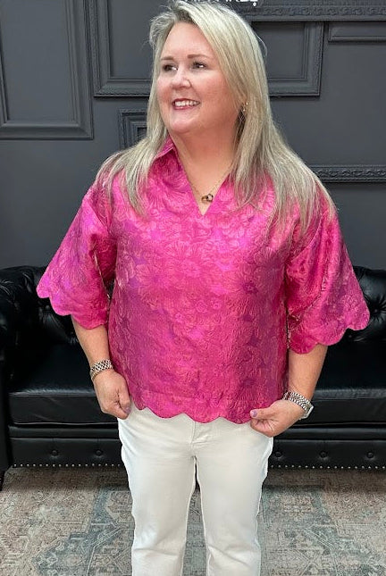 Woman wearing a pink blouse and white pants standing in a room with a black leather couch and gray walls.