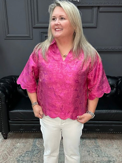 Woman wearing a pink blouse and white pants standing in a room with a black leather couch and gray walls.