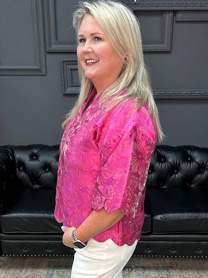 Woman in a pink blouse and white pants standing in a room with a black leather couch and gray walls.