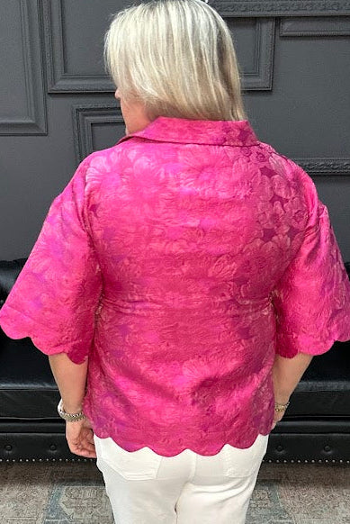 Woman wearing a pink textured blouse and white pants in a store setting.