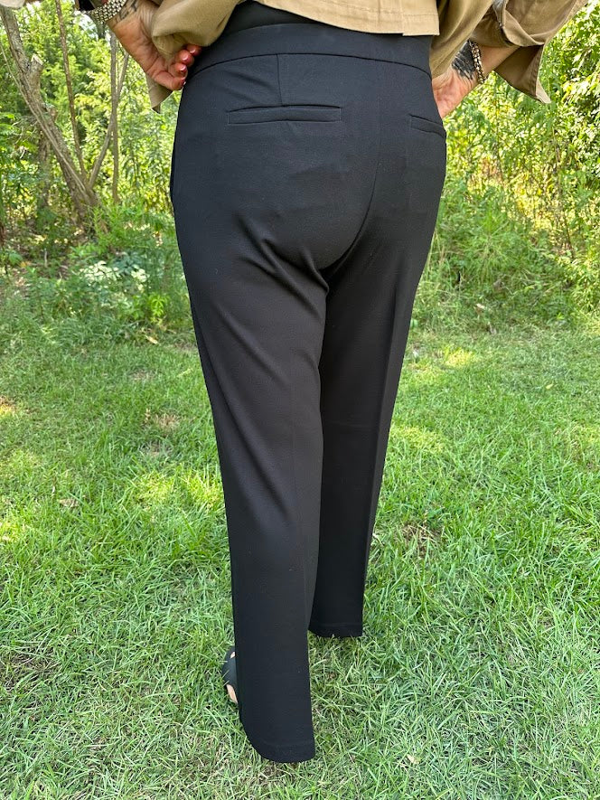 Person wearing black pants standing in a grassy area with trees in the background