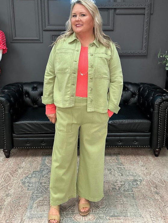 Woman in a green outfit standing in a room with a black leather couch and a neon sign.