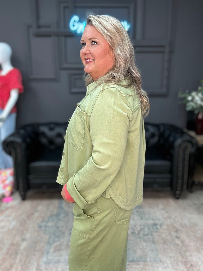 Woman in a green outfit standing in a room with dark walls and furniture.