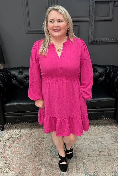 Woman in a pink dress standing in front of a Christmas tree and 'Gypsy River Apparel' sign.
