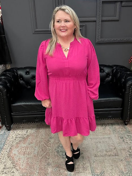Woman in a pink dress standing in front of a Christmas tree and 'Gypsy River Apparel' sign.