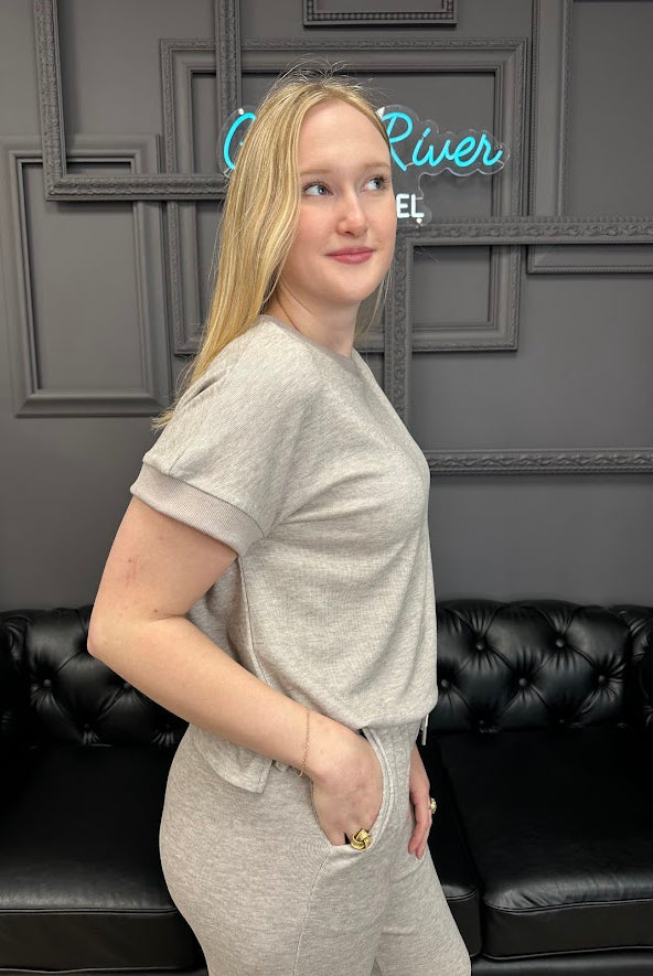 Woman in a gray outfit standing in front of a black leather couch with a decorative wall in the background.