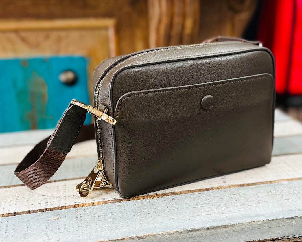 Brown leather crossbody bag on a wooden surface with a blurred background