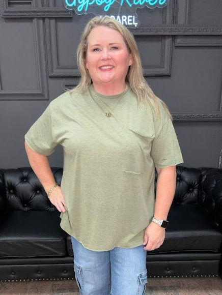 Woman wearing a green top and blue jeans standing in a room with a black leather couch and decorative items.