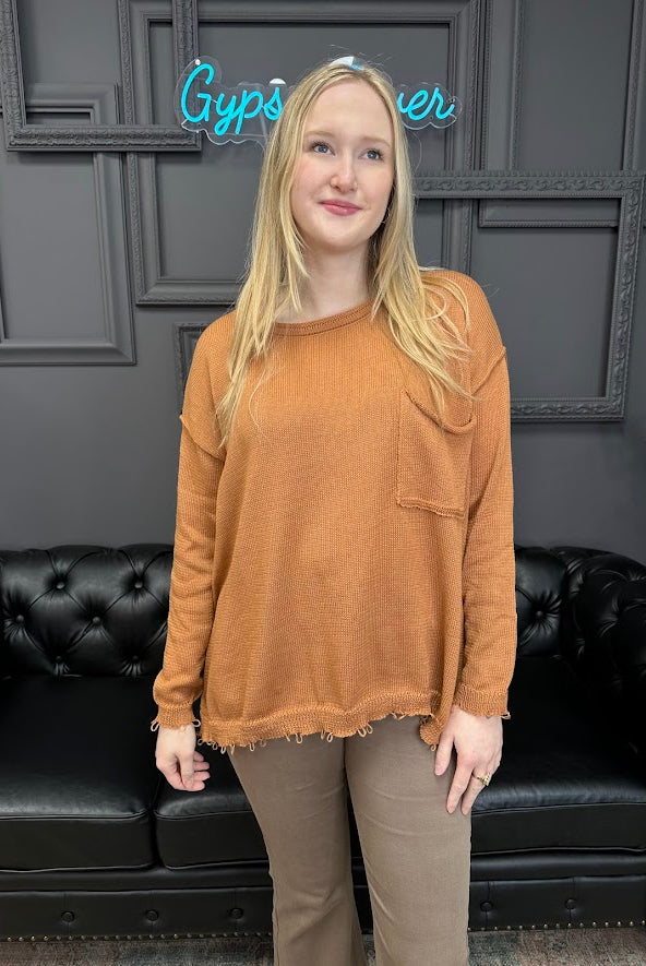 Person wearing a brown sweater standing in front of a black couch with a neon sign in the background.
