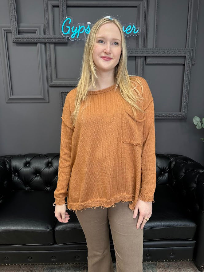 Person wearing a brown sweater standing in front of a black couch with a neon sign in the background.