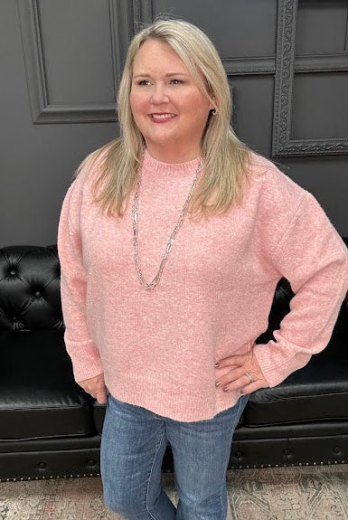 Woman wearing a pink sweater and blue jeans standing in front of a black leather couch.