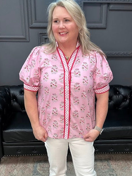 Woman wearing a pink floral blouse and white pants standing in a room with a black leather couch and gray walls.