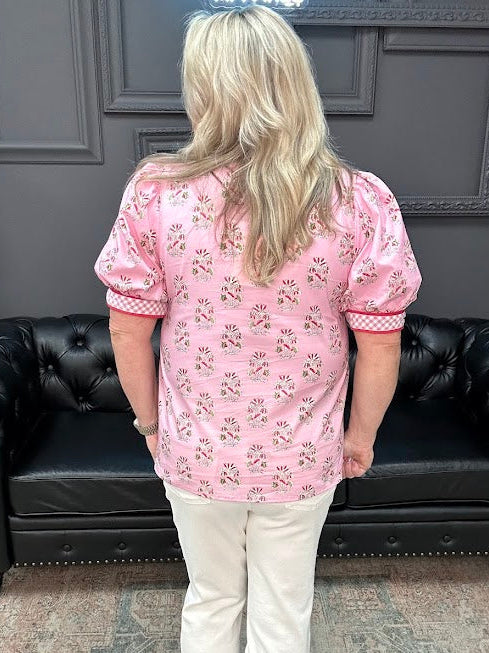 Person wearing a pink floral blouse and white pants standing in a room with a black leather couch and gray walls.