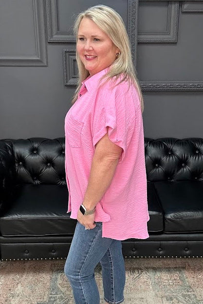Woman in a pink shirt and blue jeans standing in front of a black leather couch.