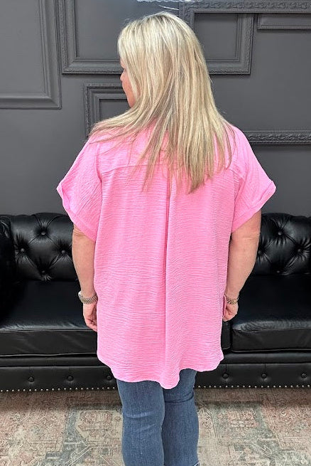 Person wearing a pink shirt and blue jeans standing in front of a black leather couch.
