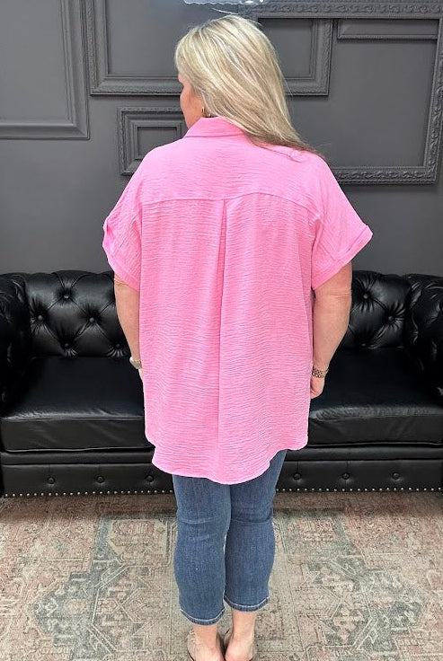 Person wearing a pink shirt and blue jeans standing in front of a black leather couch.