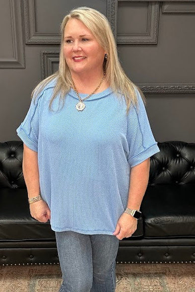 Woman in a blue shirt standing in front of a black leather couch with a dark wall and neon sign in the background.