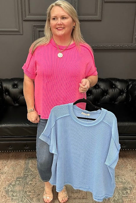 Woman holding a blue shirt in front of a black leather couch with a gray wall background.