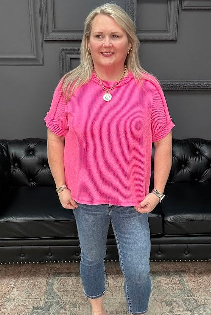 Woman in a pink shirt and blue jeans standing in front of a black leather couch.