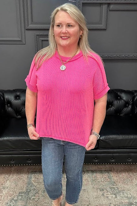 Woman in a pink shirt and blue jeans standing in front of a black leather couch.