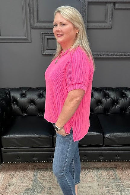 Woman in a pink shirt and jeans standing in front of a black leather couch.