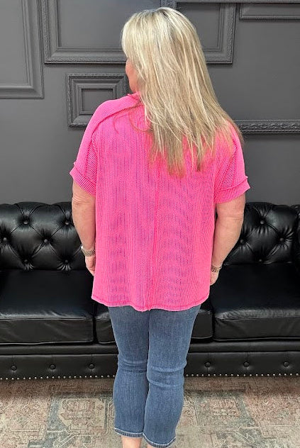 Person wearing a pink shirt and blue jeans standing in front of a black leather couch.