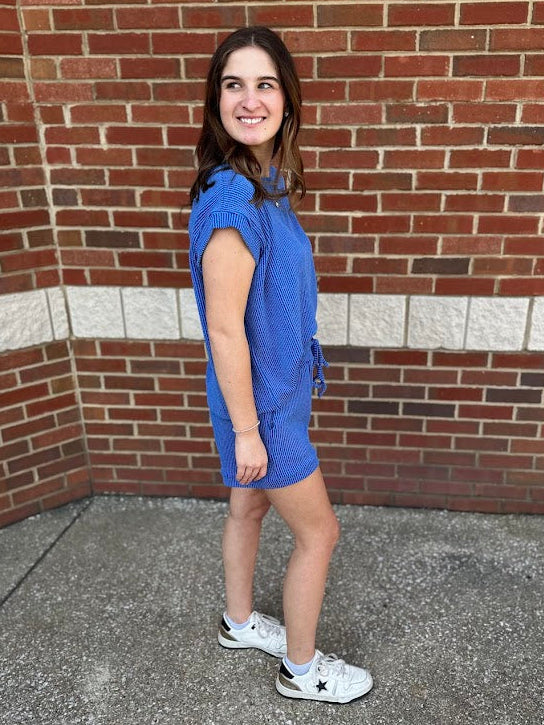 Woman in a blue dress standing against a brick wall