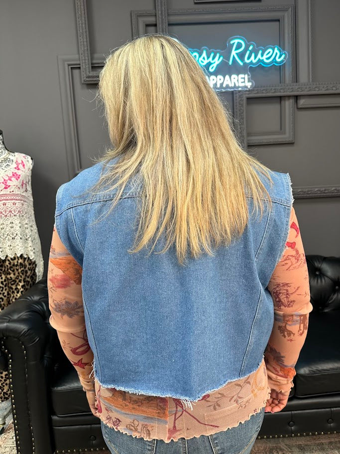 Person wearing a denim vest with tattoos visible on arms, standing in front of a store with a neon sign.