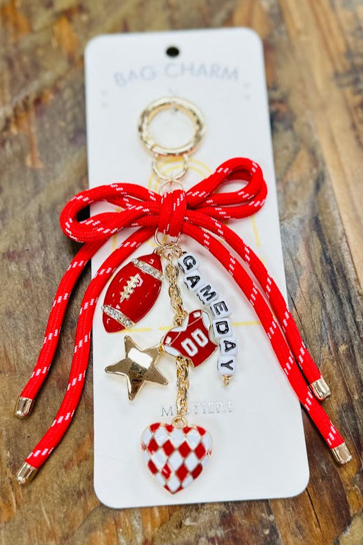 Red and gold bow keychain with charms on a white card against a wooden background