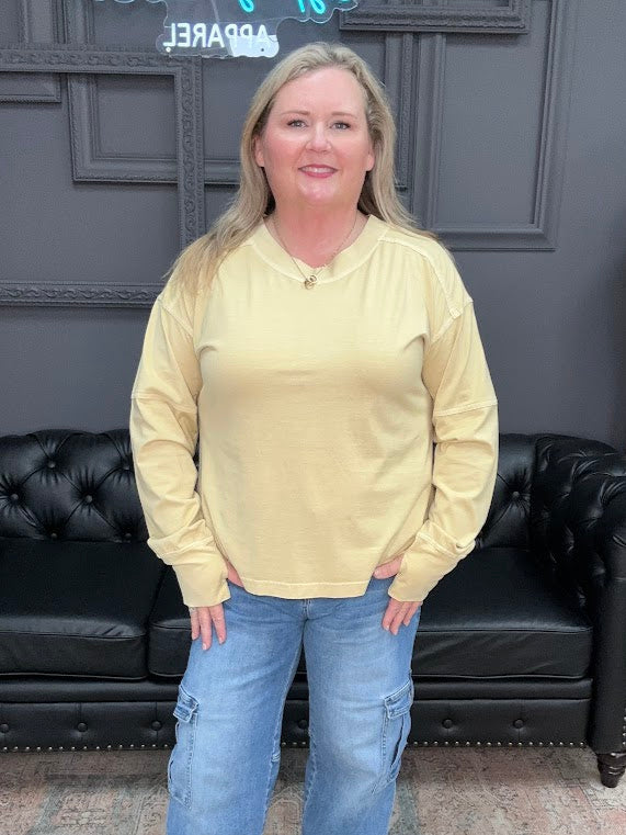 Woman wearing a yellow long-sleeve shirt and blue jeans standing in front of a black leather couch.