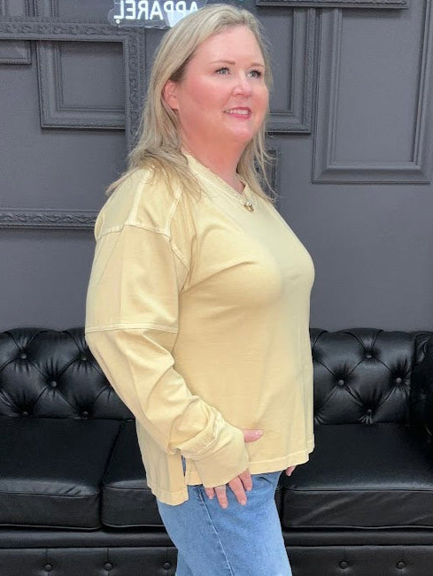 Woman wearing a yellow jacket and blue jeans standing in a room with black leather couches and a patterned rug.